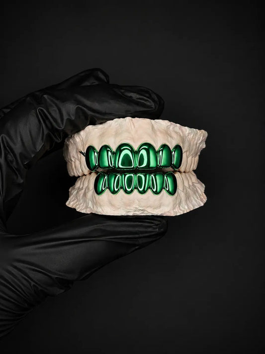 Grillz with green accents held by a gloved hand against a black background