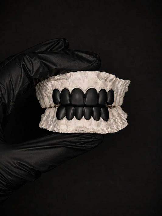 Black dentures held by a gloved hand against a black background