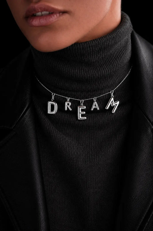 Person wearing a black turtleneck with a necklace featuring the word 'DREAM'.