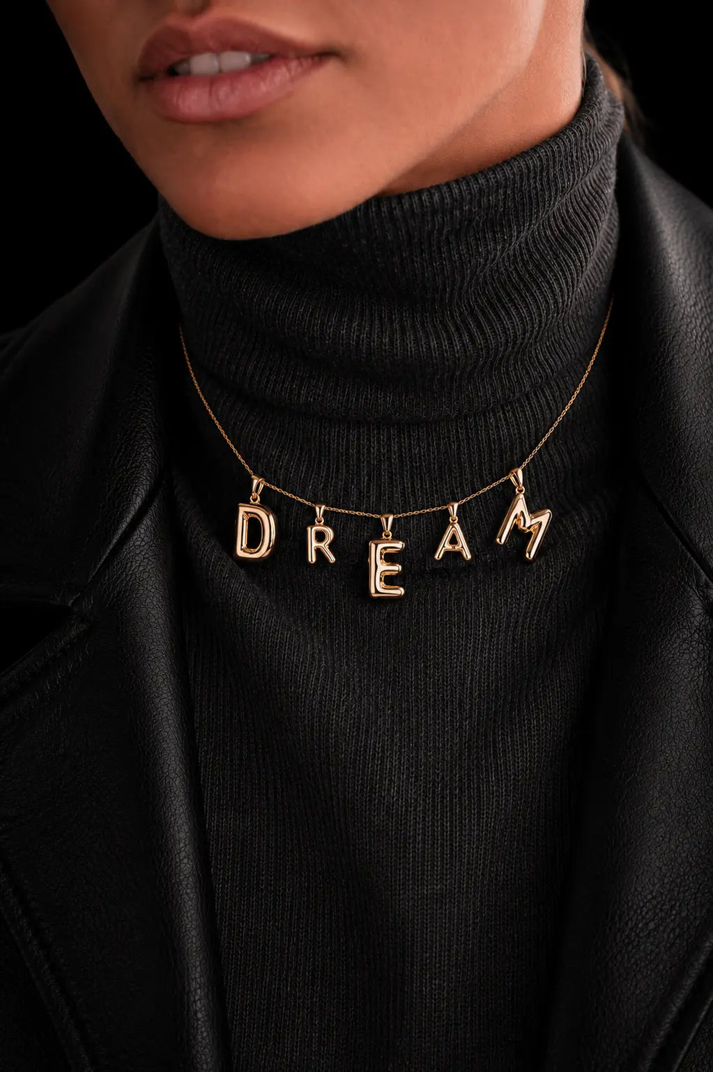 Gold necklace with 'DREAM' pendant on a black turtleneck sweater.