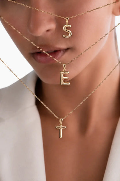 Close-up of a person wearing gold necklaces with 'S', 'E', and 'T' pendants.