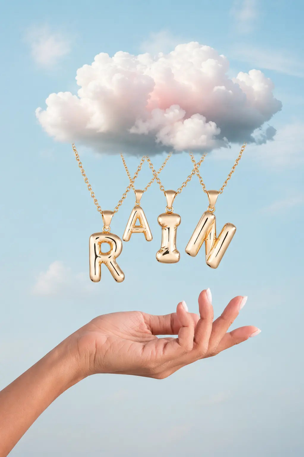 Gold necklace with 'RAIN' pendant held by a hand against a blue sky background