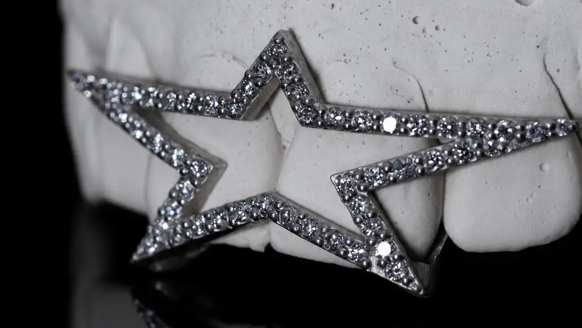A silver-toned star-shaped dental mouthguard with pavé-set clear rhinestones, shown fitted over a white dental mold on a reflective black surface.
