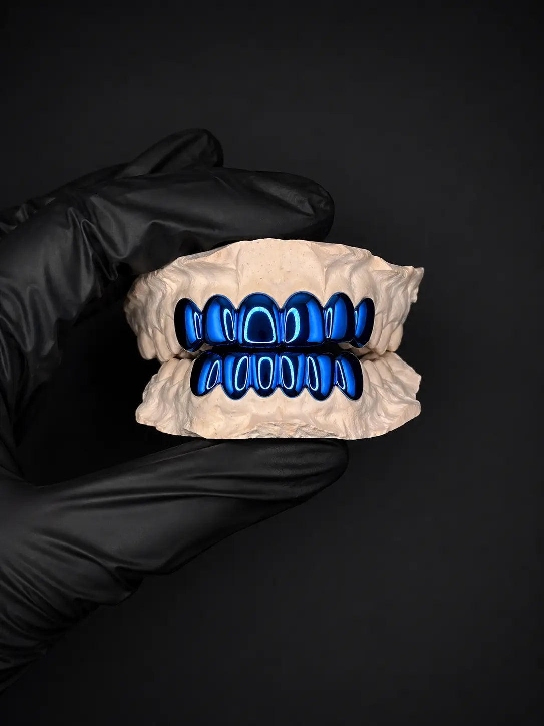 Dental model with blue teeth held by a gloved hand on a black background