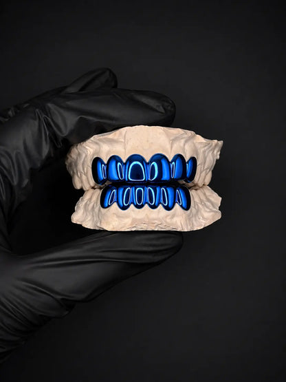 Dental model with blue teeth held by a gloved hand on a black background