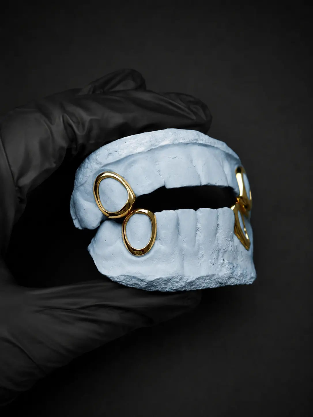 Custom gold open face grillz on a white dental model held with a black glove against a dark background