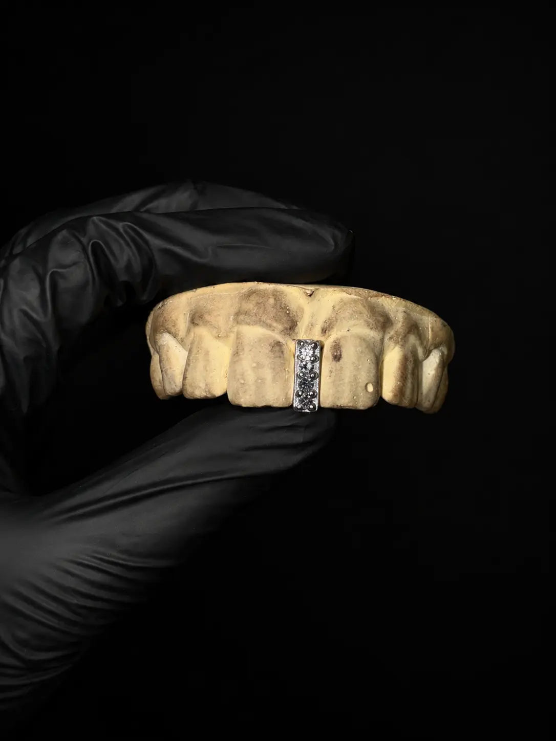 Handmade iced out diamond gap grillz with custom gemstone tooth cap displayed on black background with black gloves