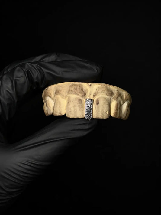 Handmade iced out diamond gap grillz with custom gemstone tooth cap displayed on black background with black gloves