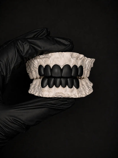 Black dentures held by a gloved hand against a black background