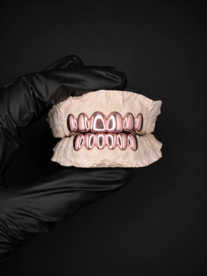 Hand wearing a black glove holding a set of rose gold dental aligners against a black background