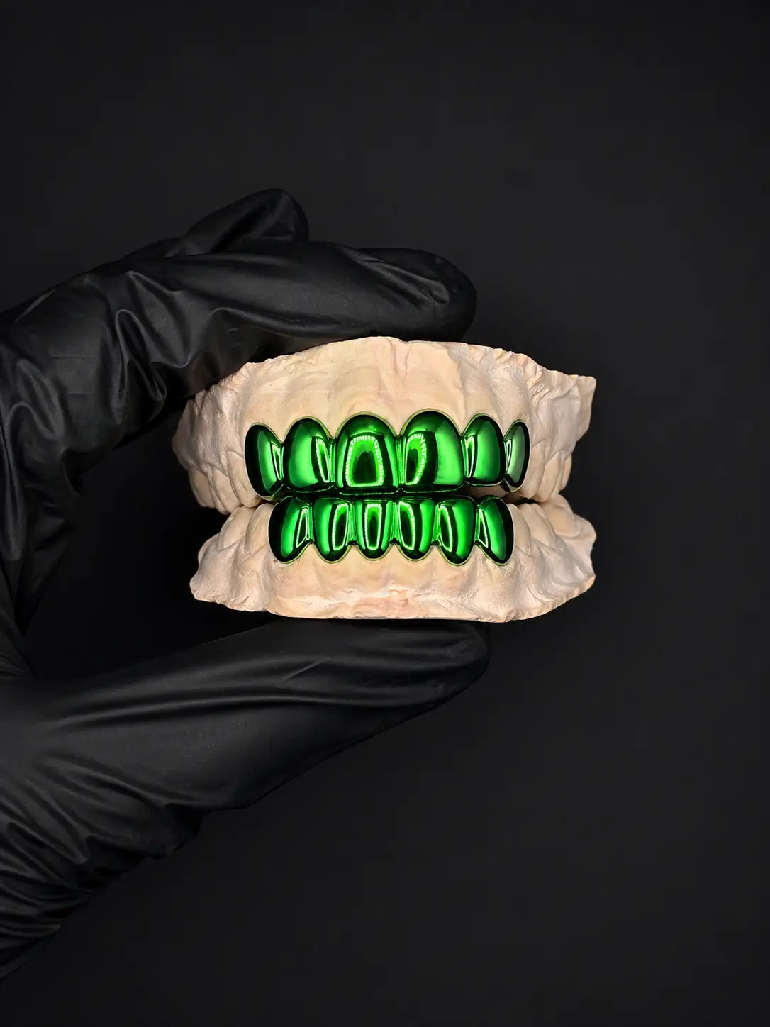 Gloved hand holding a set of green teeth on a black background