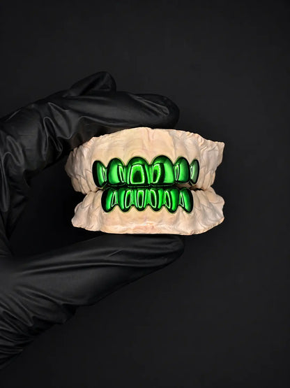 Gloved hand holding a set of green teeth on a black background