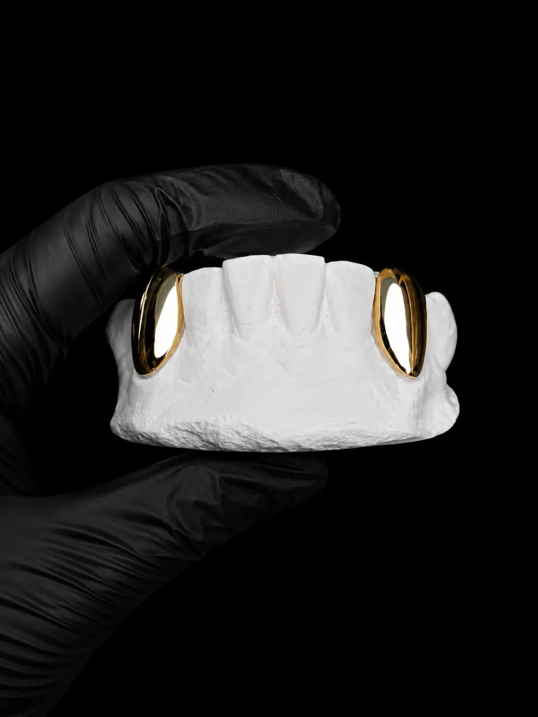 Custom single gold tooth grill on a dental mould with black background and black glove