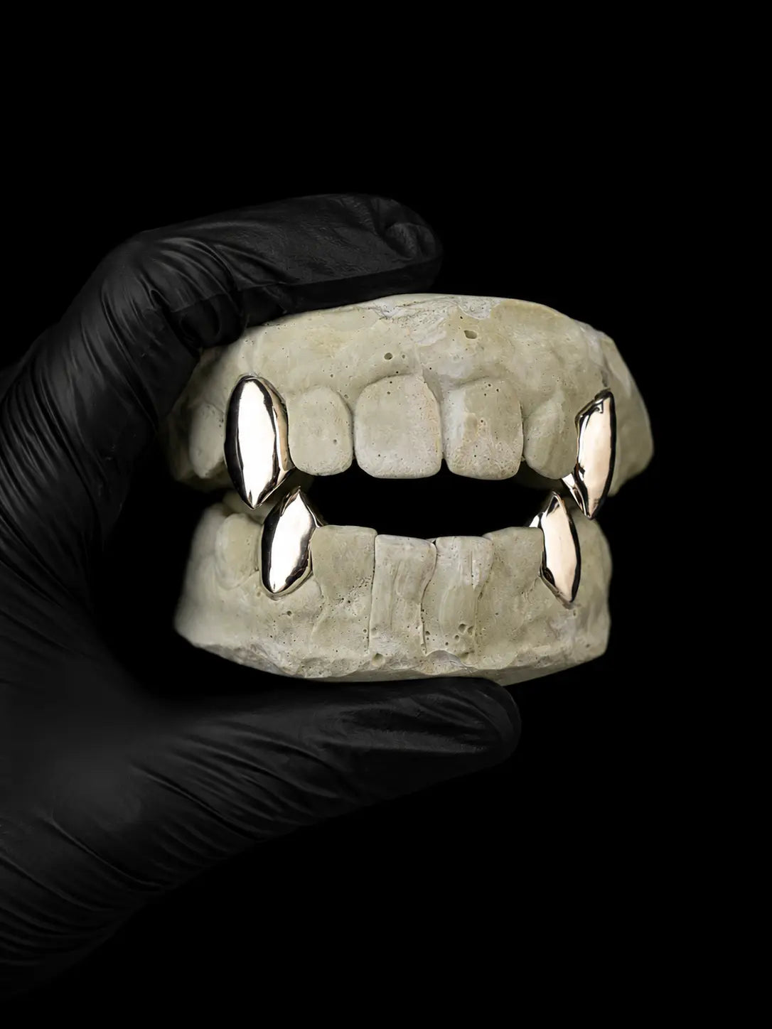 Custom vampire fang grillz in silver on dental mould with black glove and black background