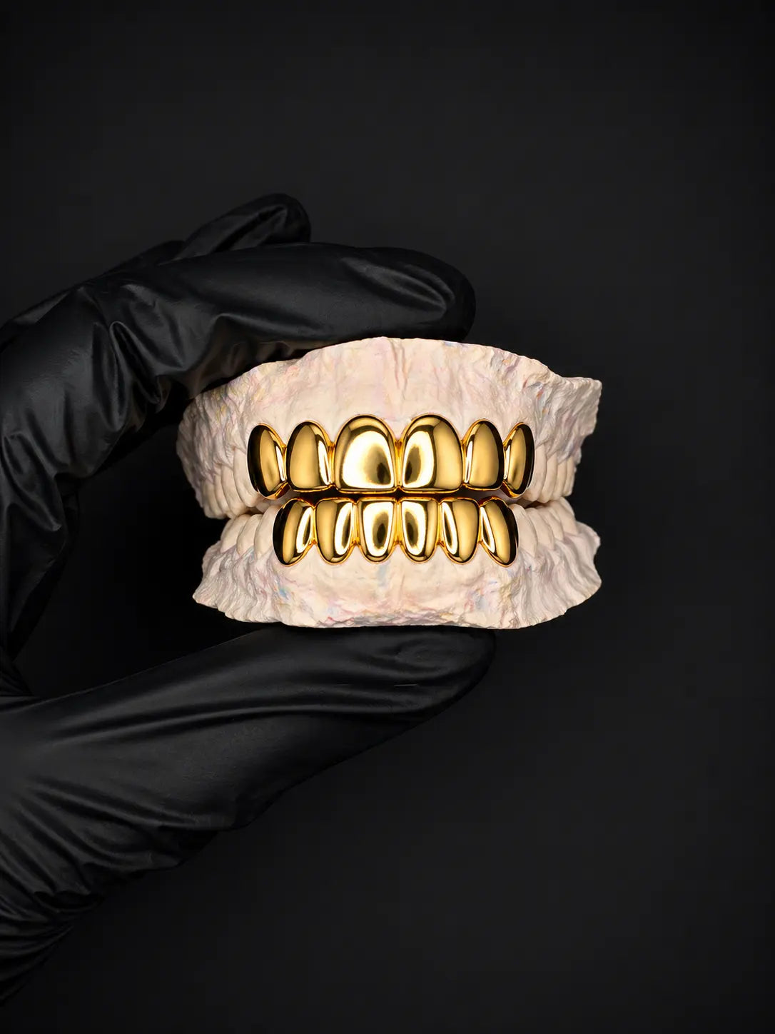 Gold grillz on a white background held by a gloved hand