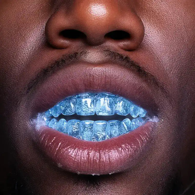 Close-up of a person's mouth with blue teeth and ice cube grillz
