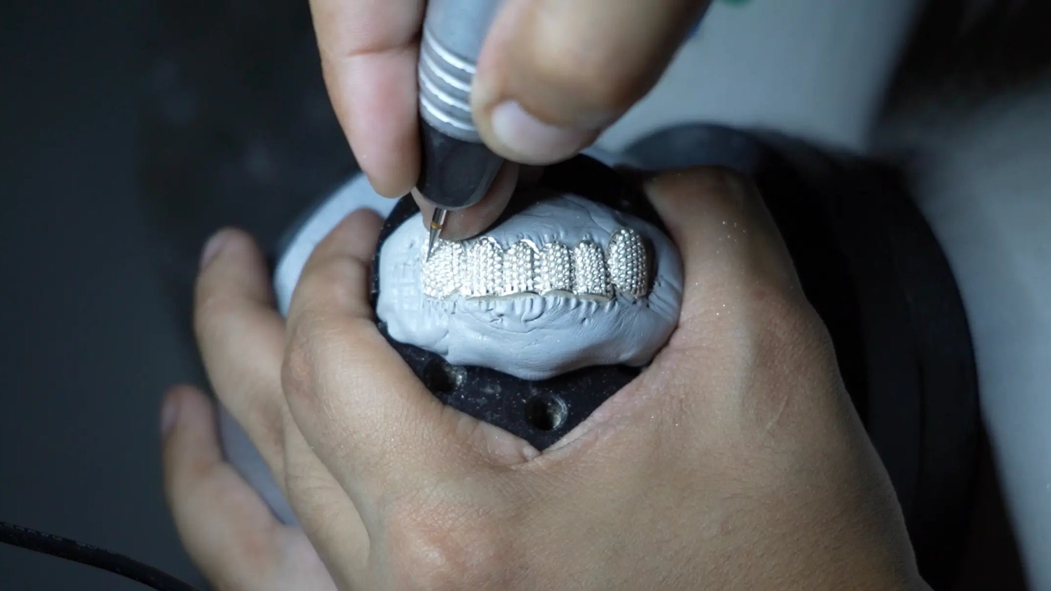 Close-up of hands using a tool on a small mechanical component.