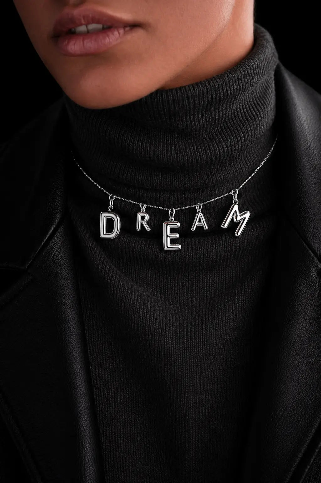 Person wearing a black turtleneck with a necklace featuring the word 'DREAM'.