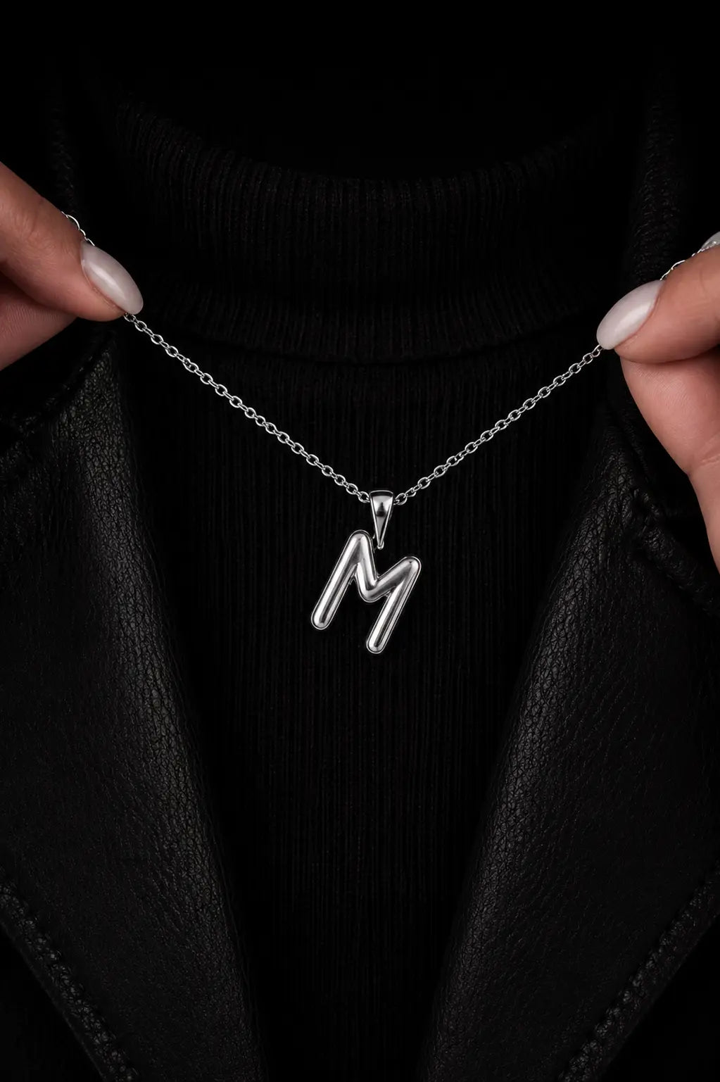 Silver necklace with a 'M' pendant held against a black background
